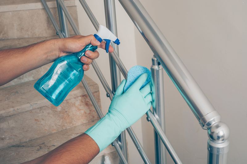 Gloved hand disinfecting a stair handrail